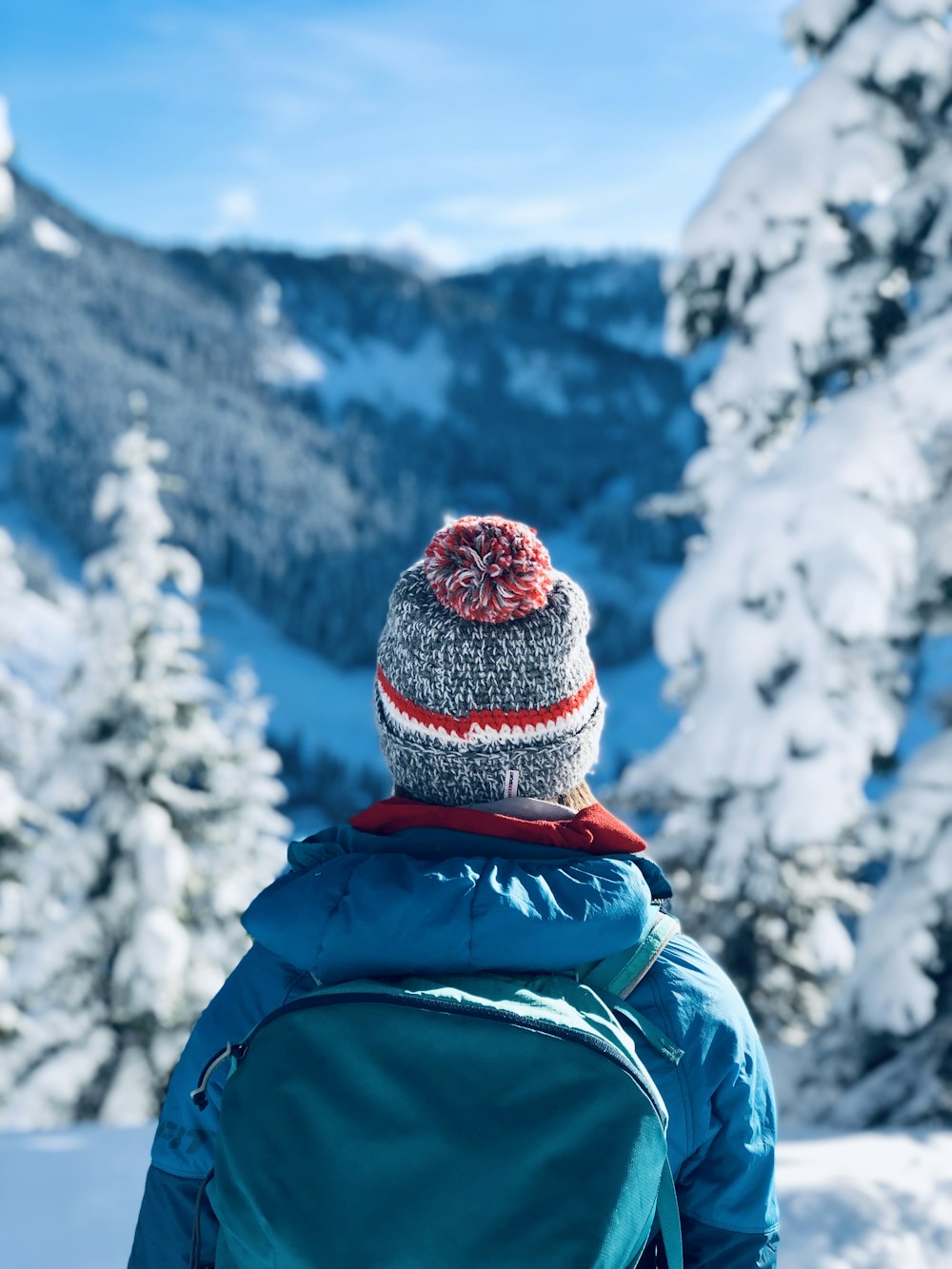 person wearing gray bobble knit cap and blue jacket with backpack