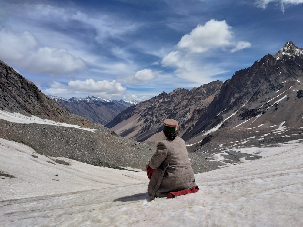 person sitting on snow field facing on mountain during daytime