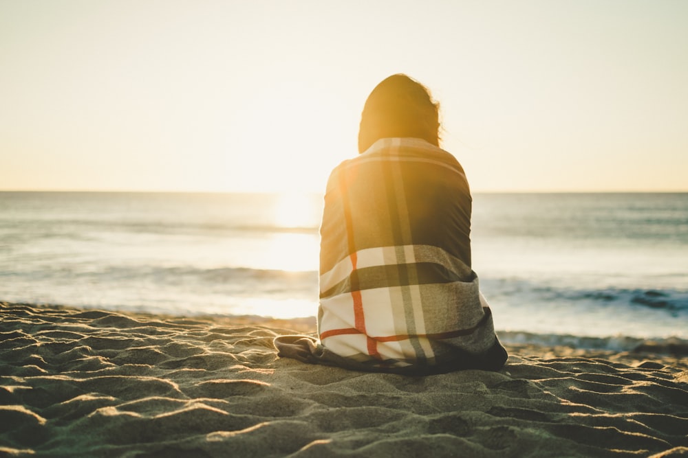 woman sitting on brown sand covered with blanket