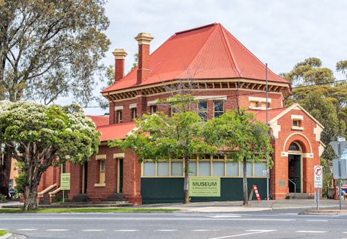 A historic red-brick building with a triangular roof and tall chimneys, surrounded by trees and located at a street corner. This building houses a museum and research center, as indicated by the signs. The entrance features an arched doorway, and the exterior is decorated with lush greenery.