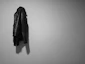 Minimalist shot of a black leather motorcycle jacket hanging against a gray wall with subtle red lighting.