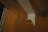 A shadow is cast on a wall in a dimly lit room, creating geometric patterns from the interaction of light and architecture. The shadow appears to be of a person holding a camera, adding an element of mystery to the scene.