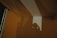 A shadow is cast on a wall in a dimly lit room, creating geometric patterns from the interaction of light and architecture. The shadow appears to be of a person holding a camera, adding an element of mystery to the scene.