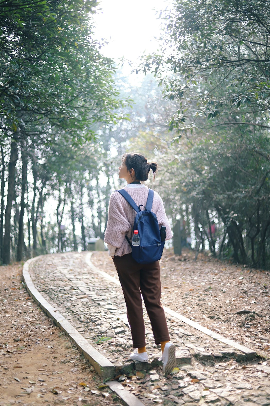 woman walking on concrete pathway near trees during daytime