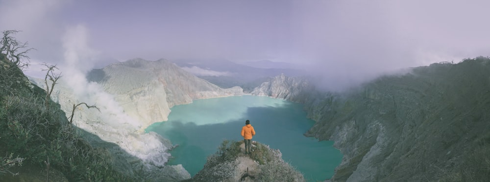 panoramic photography of person standing on cliff during daytime
