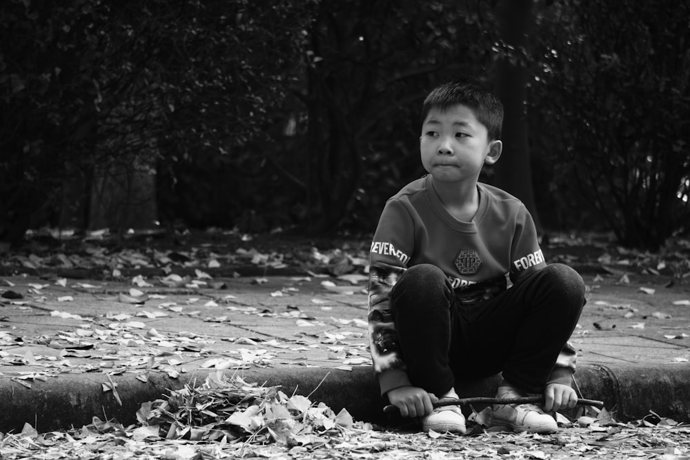 grayscale photography of boy sitting on concrete road