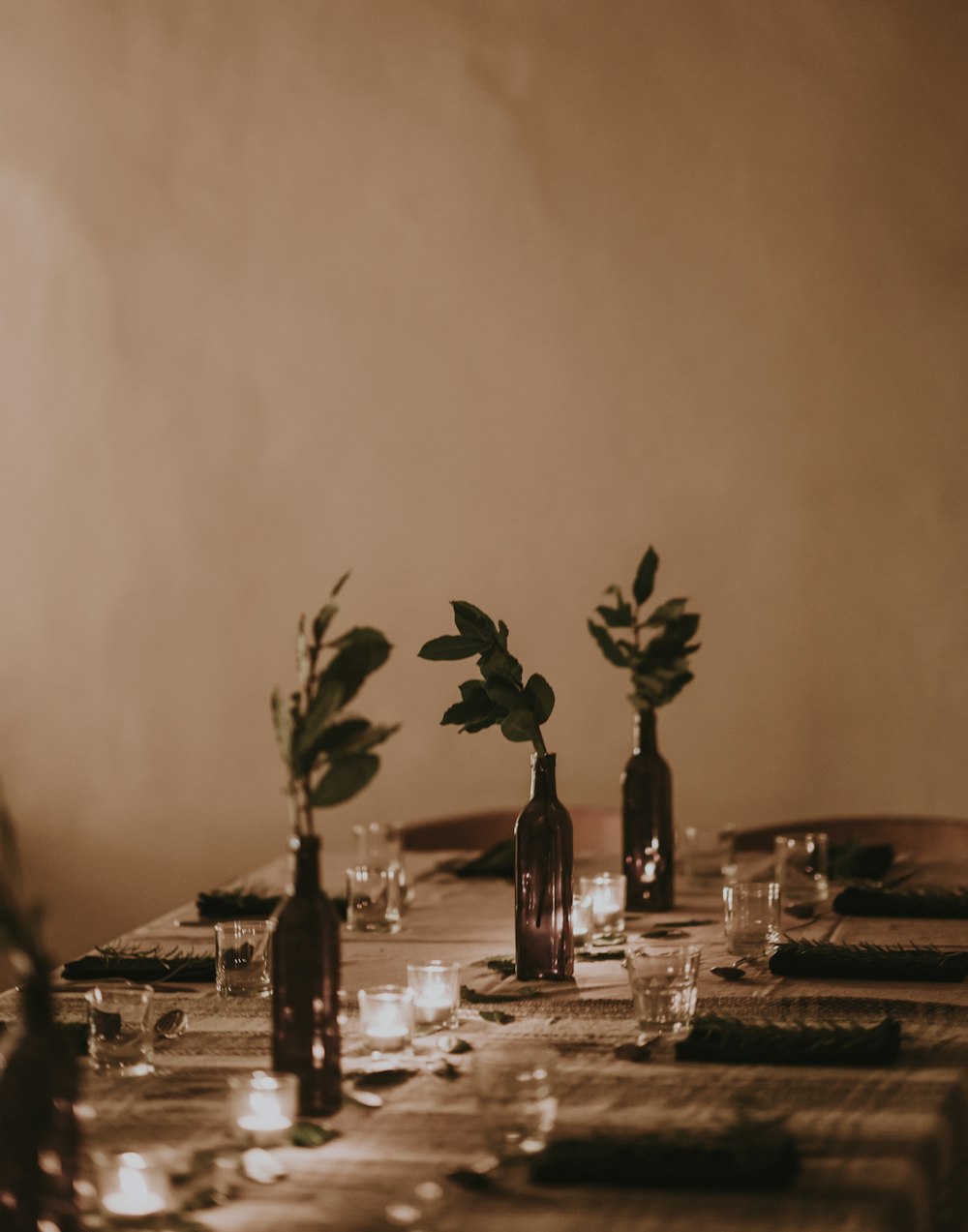 Pflanzen in Flaschenvasen von eingeschalteten Teelichtern auf dem Tisch