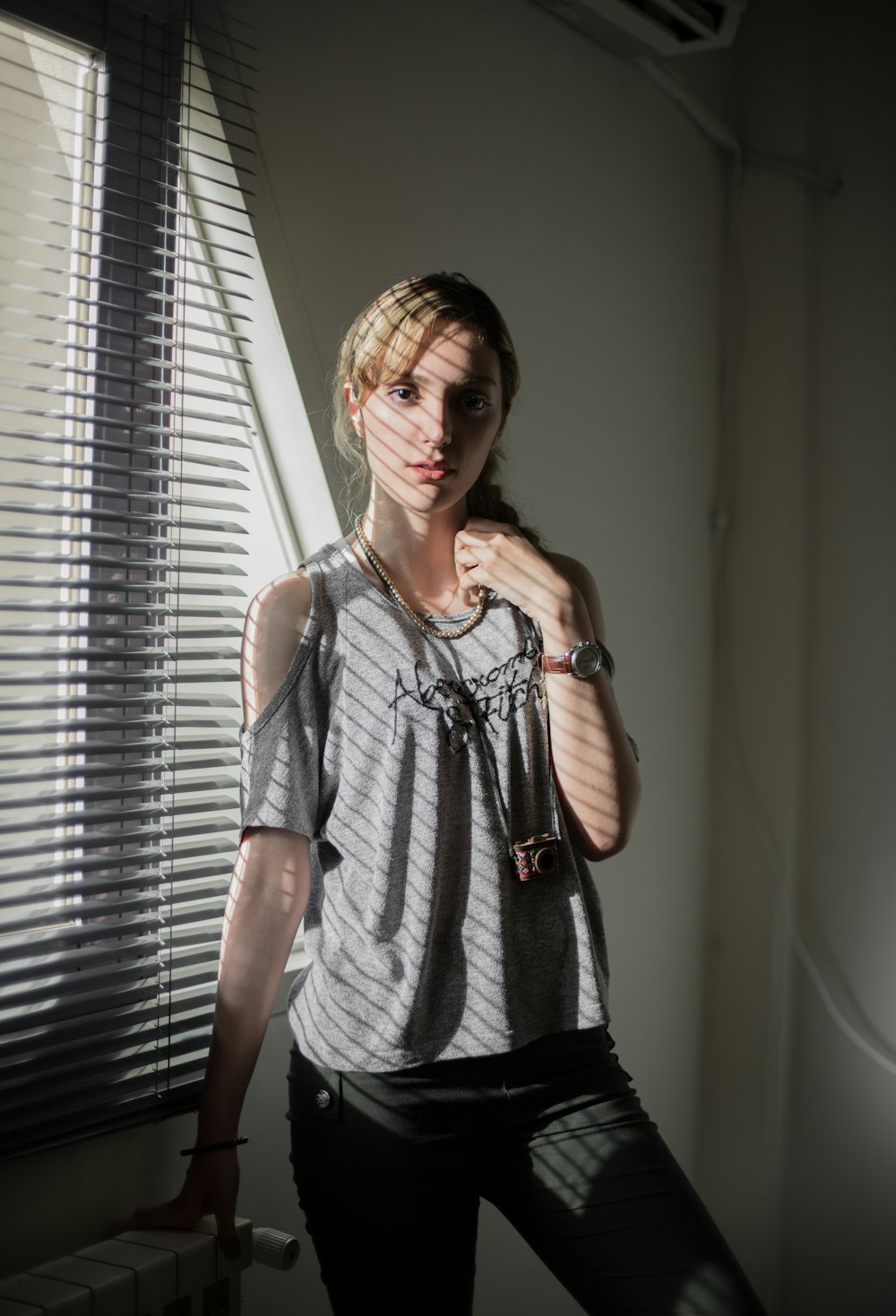 woman in gray cold shoulder top standing near window with blinds