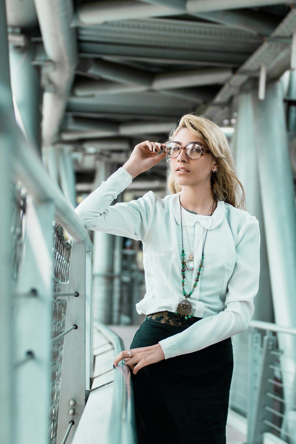 woman standing and touching eyeglasses near railings