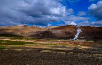 A panoramic view of the Krafla geothermal power plant with steam rising against a rugged volcanic landscape.