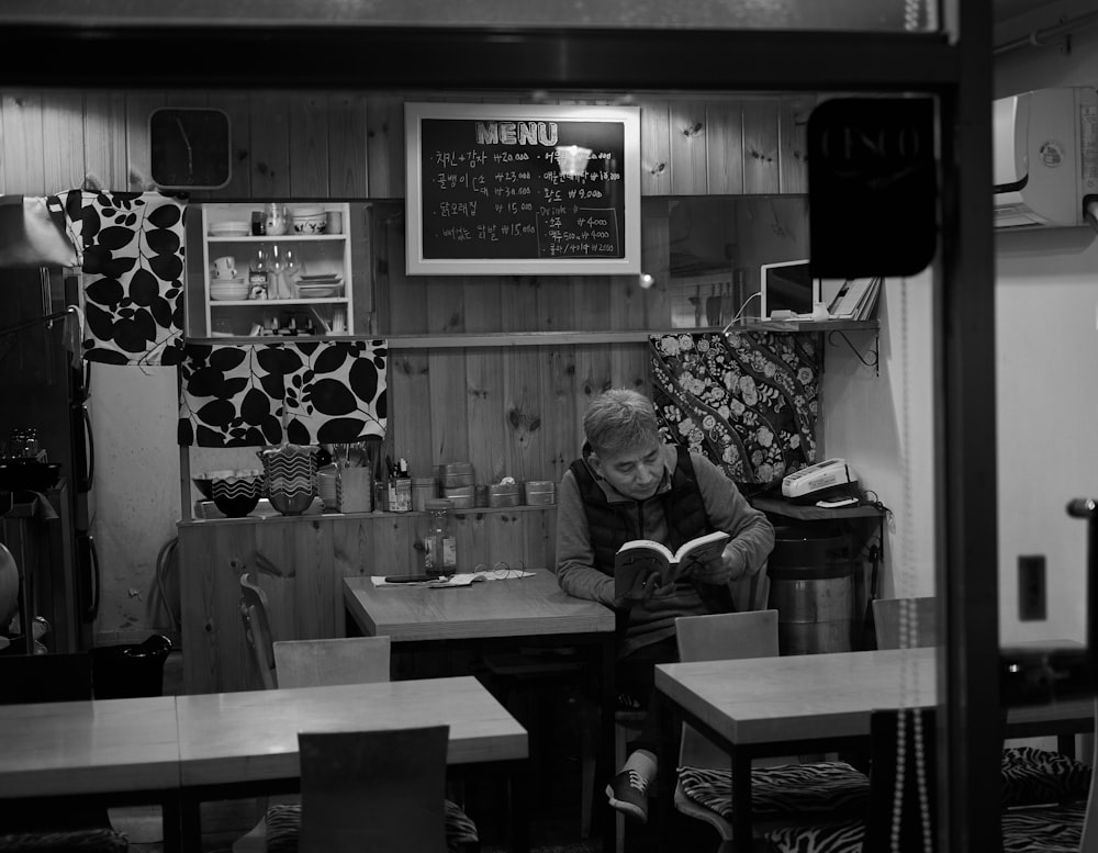 man reading book while sitting on chair inside room