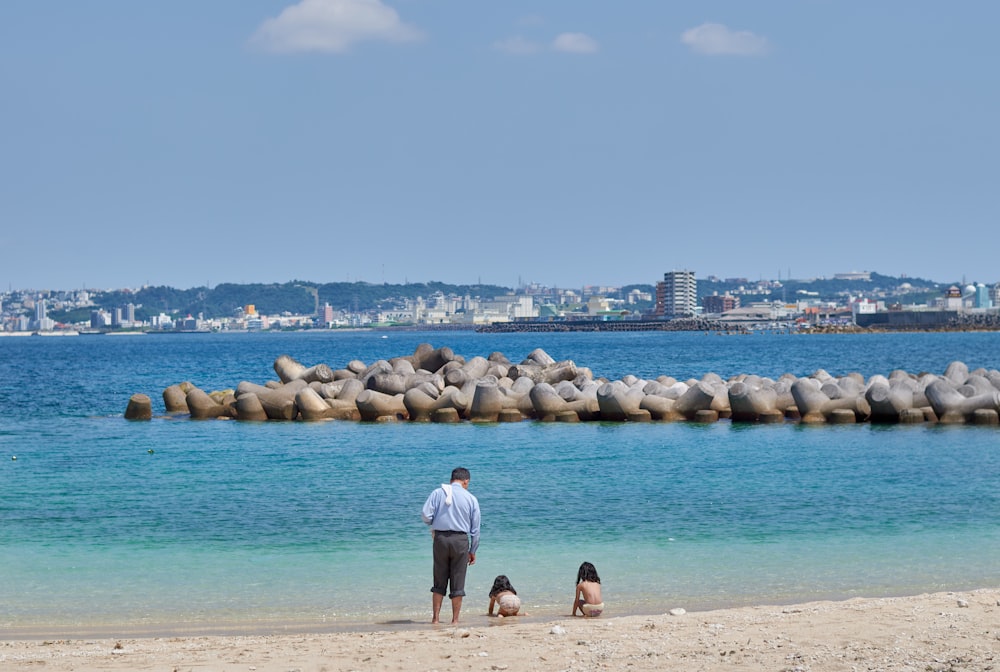 man standing on beach shoreline beside two girls at daytime