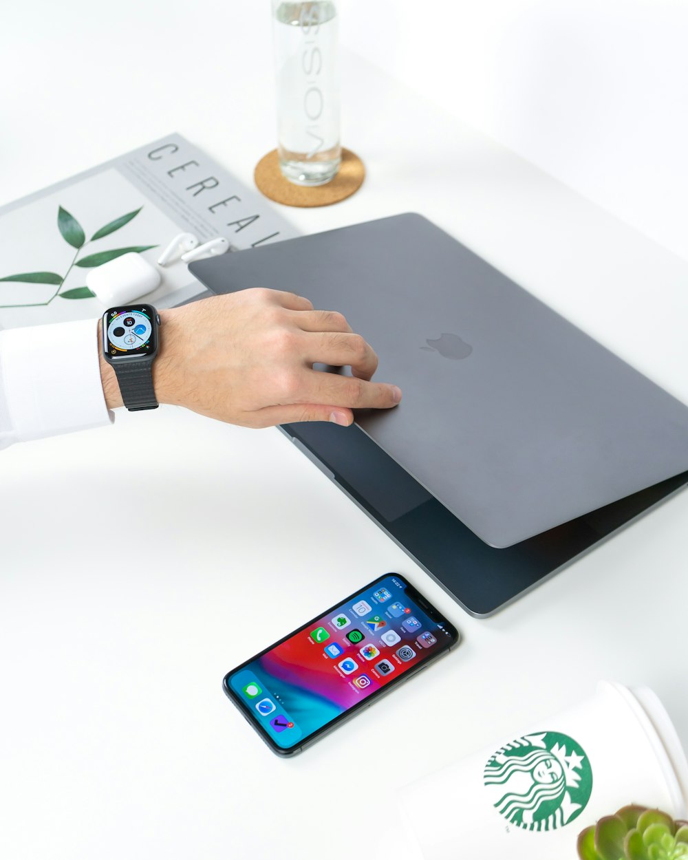白い木製のテーブルの上でiPhoneの横で灰色のMacBookを開く人
