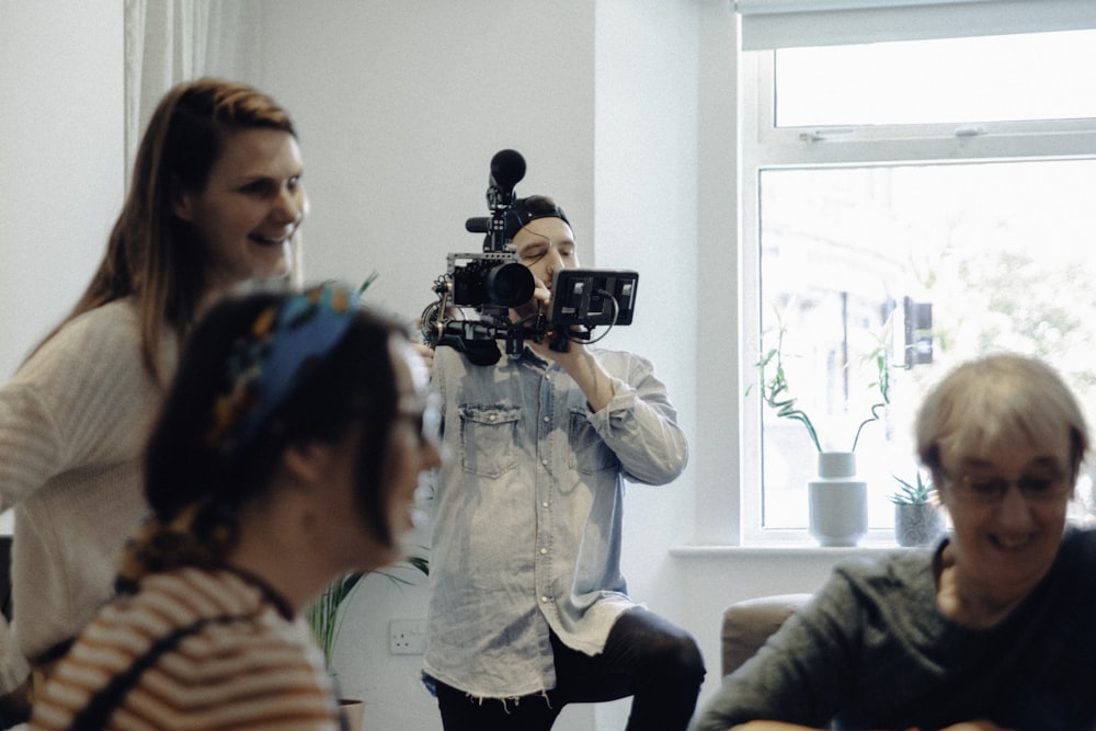 people standing inside room while man standing and holding recording camera during daytime