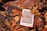 An e-reader with a low battery symbol is nestled among brown and yellow autumn leaves on a textured wooden surface.