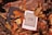 An e-reader with a low battery symbol is nestled among brown and yellow autumn leaves on a textured wooden surface.