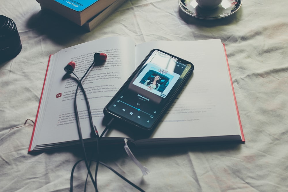 black Android smartphone with plugged-in earphones on book