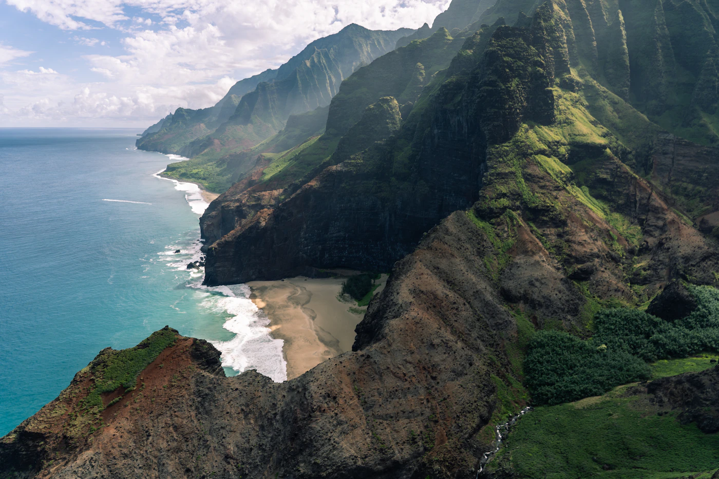 Dramatic view of Kaua'i's Na Pali Coast with jagged emerald cliffs meeting the blue Pacific