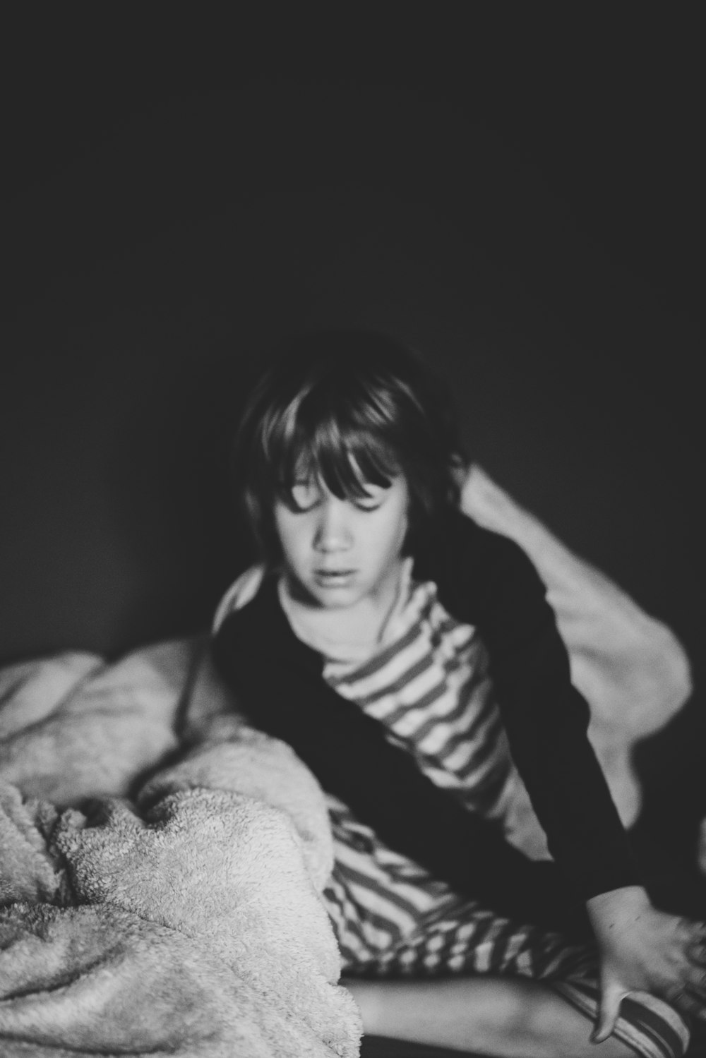 child sitting beside blanket grayscale photo