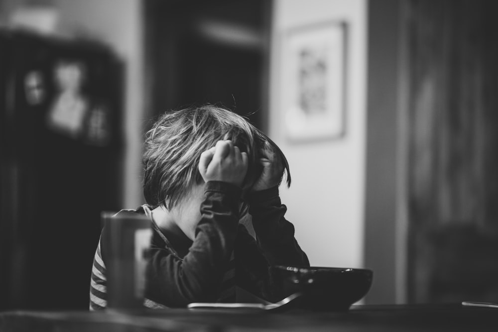 grayscale photography of boy sitting beside table