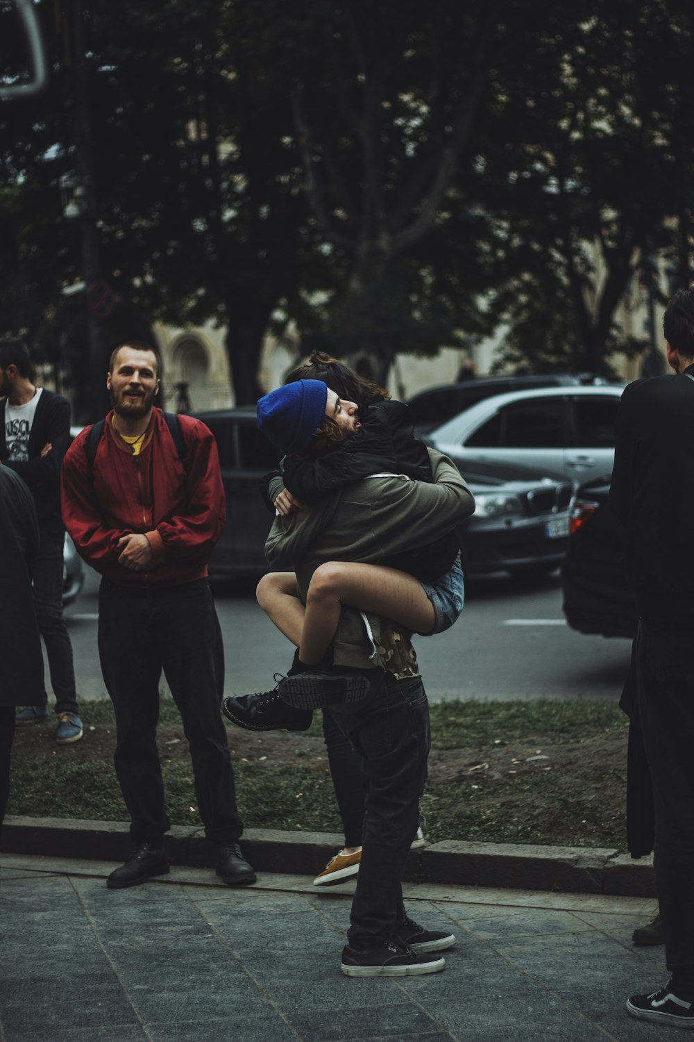 man hugging woman while standing on sidewalk at daytime
