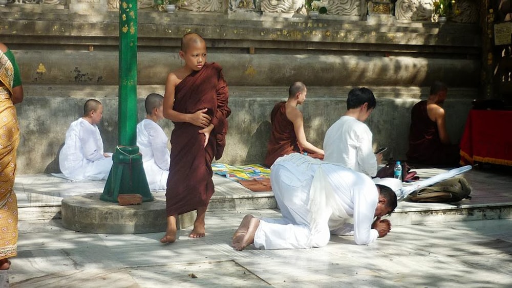 man kneeling on ground beside monk at daytime