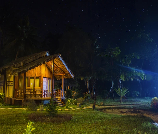 Cozy wooden bungalow nestled among lush tropical plants at sunset.