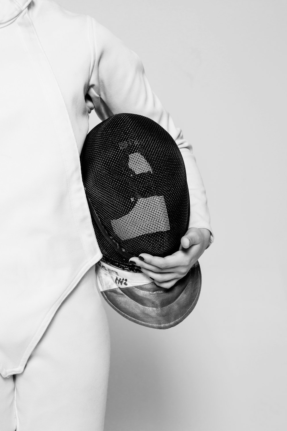 person wearing white fencing suit holding black mask inside room