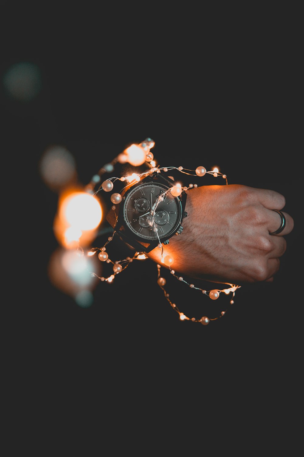 person wearing round black chronograph watch and string lights