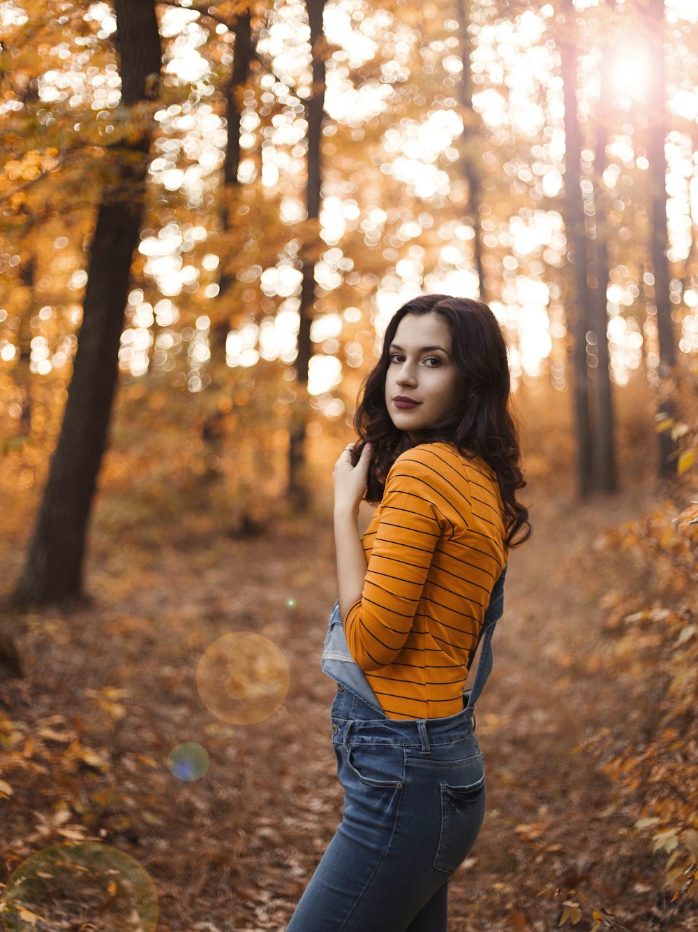 woman wearing blue jeans standing under brown trees