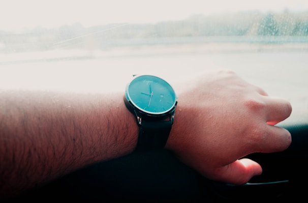 Person wearing a sleek watch while driving, with urban architecture blurred in the background