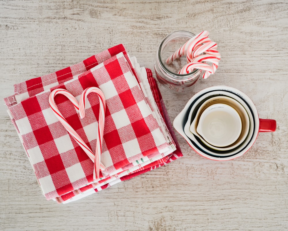 white ceramic mugs beside red and white checked textile
