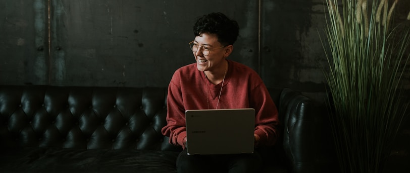 smiling man using laptop computer while sitting on black leather sofa