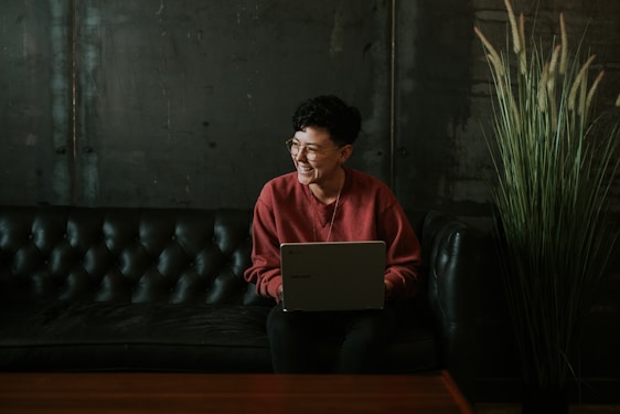 smiling man using laptop computer while sitting on black leather sofa