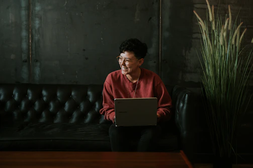 smiling man using laptop computer while sitting on black leather sofa