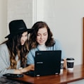 two woman sitting near table using Samsung laptop