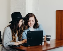 two woman sitting near table using Samsung laptop