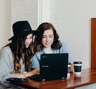 two woman sitting near table using Samsung laptop