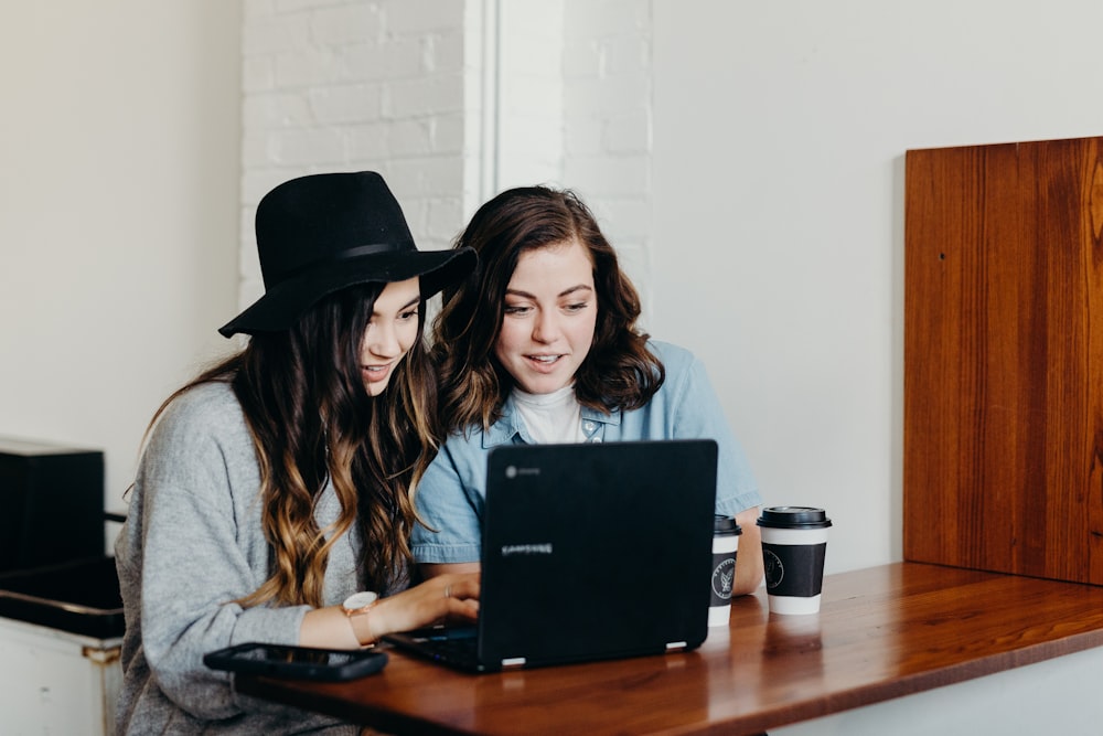 dos mujeres sentadas cerca de la mesa usando una computadora portátil Samsung