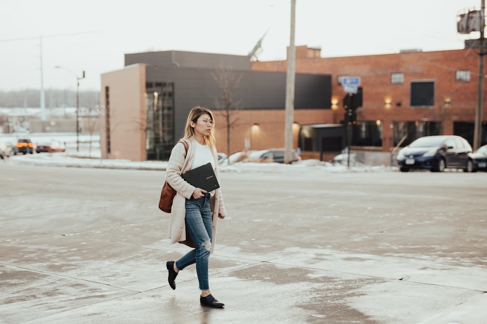 woman wearing beige cardigan carrying laptop while walking during daytime