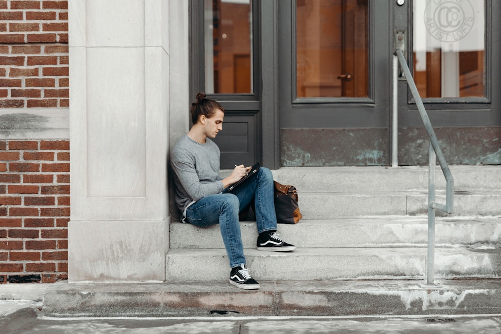 man wearing top sitting on concrete stair leaning on wall during daytime