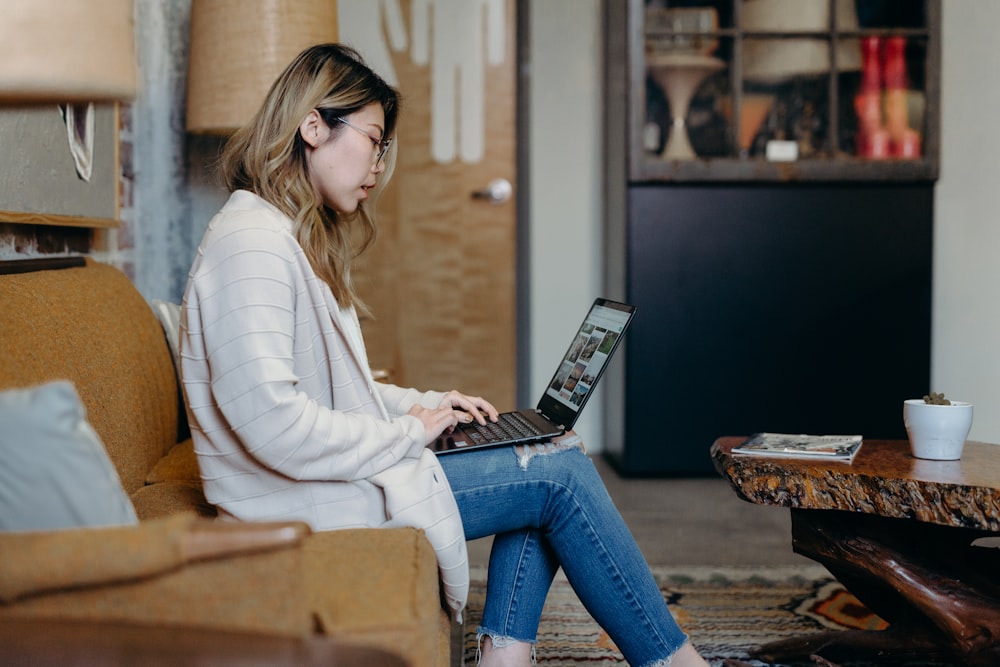 Frau benutzt Laptop, während sie auf einem Sofasessel sitzt