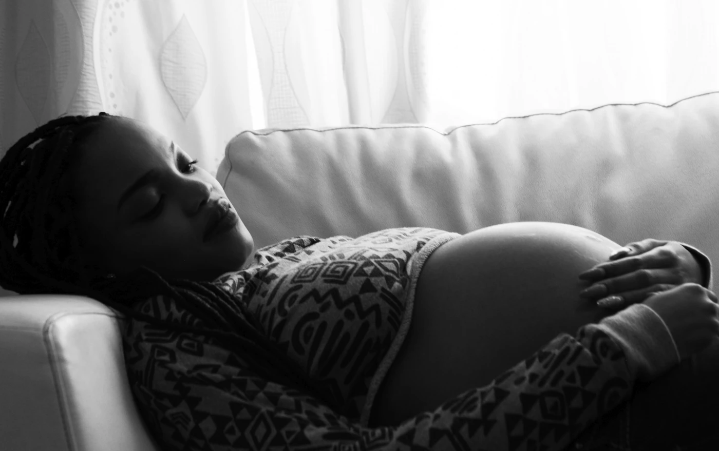 Future maman se reposant sur un canapé avec des coussins dans une pièce naturelle