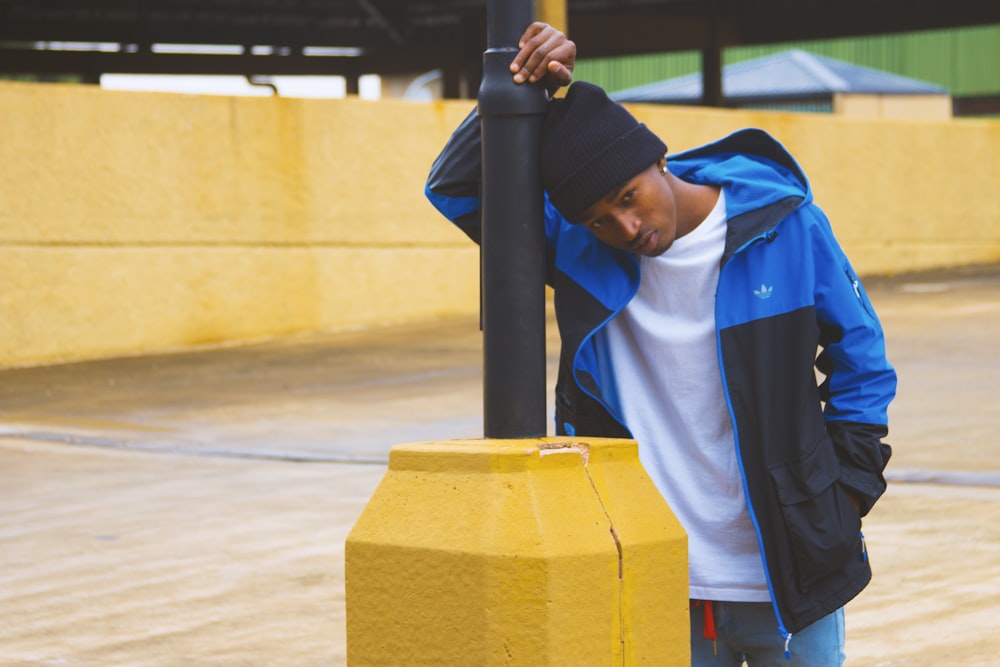 man in bue and black jacket leaning on black and yellow pole