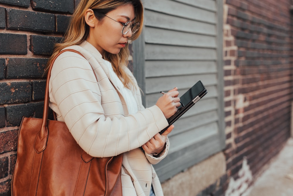 mulher apoiada na parede enquanto usa tablet