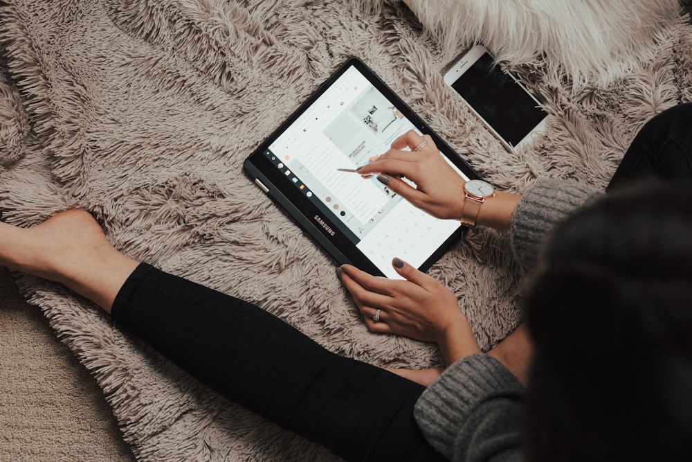 woman wearing black leggings lying on rug using tablet