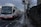 A bus marked with 'Bus Éireann' is traveling on a road with designated bicycle lanes. The sky is overcast, and there is a leafless tree on the right-hand side near a stone wall. A person is walking on the sidewalk near a traffic light pole.