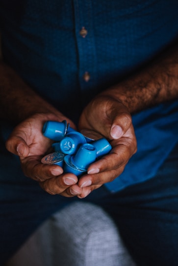 A pair of hands holding multiple blue coffee capsules, with a dark blue shirt visible in the background.