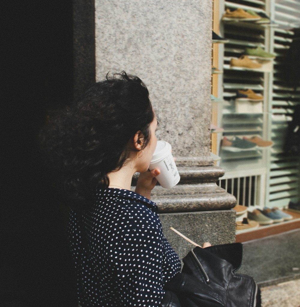 woman wearing black and white polka-dot shirt drinking white cup