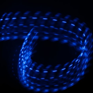 A series of bright blue lights create a looping, spiral pattern against a dark background. The lights appear to be moving, producing a glowing, dynamic effect.